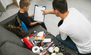 Man and child sitting on a couch with tools and items, pointing at a clipboard.